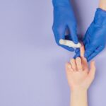 Medical professional using a glucose meter for a blood test against a pastel background.
